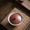 Clay teapot lid on textured wooden tray.