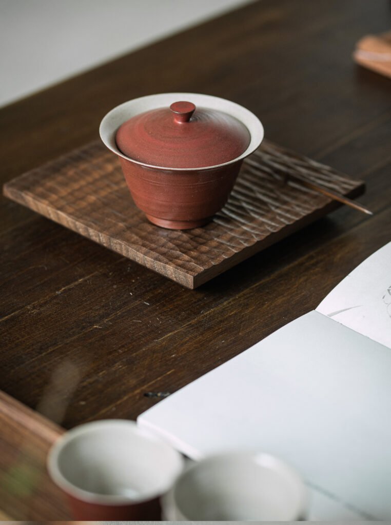 Clay teacup on wooden tray with open notebook.