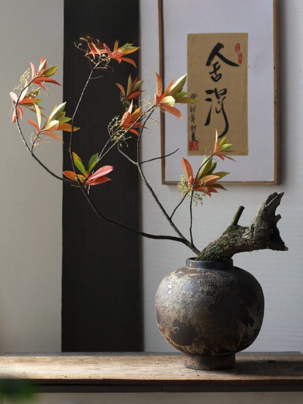 Rustic vase with branches and autumn leaves.
