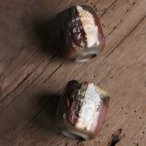 Ceramic cups with intricate Buddha faces on wooden table.