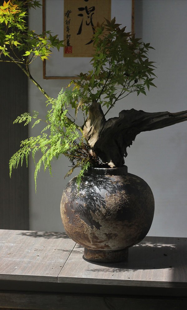Rustic vase with branches and leaves on table.