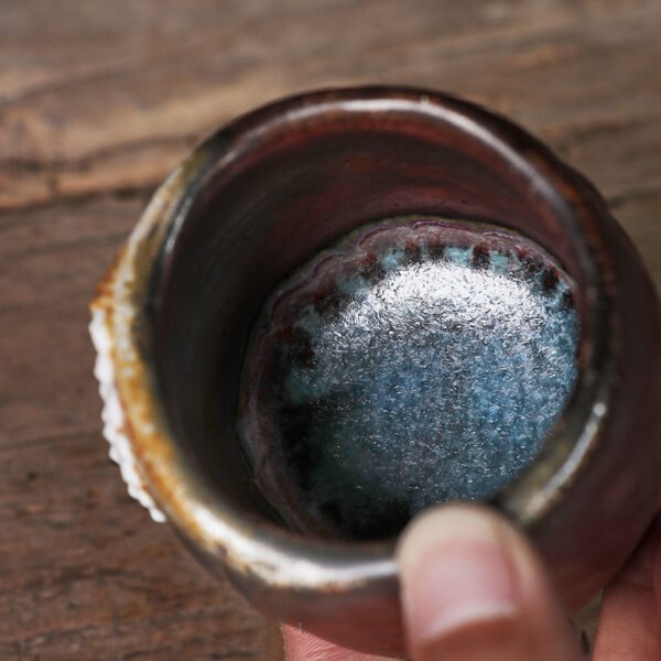 Hand holding rustic ceramic cup with blue glaze interior.