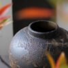 Textured dark ceramic vase with blurred plants
