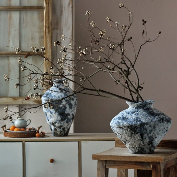 Rustic vase with branches in cozy room decor.