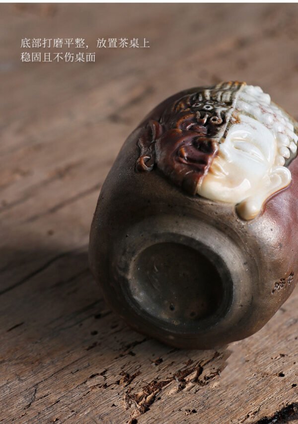 Ceramic cup with half Buddha face on table.