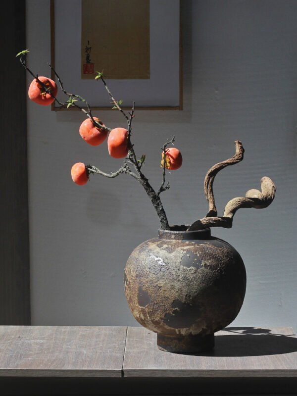 Rustic vase with persimmons on branches.