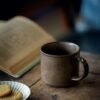 Rustic mug with biscuits beside open book.