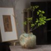 Ceramic vase with green branches on table.