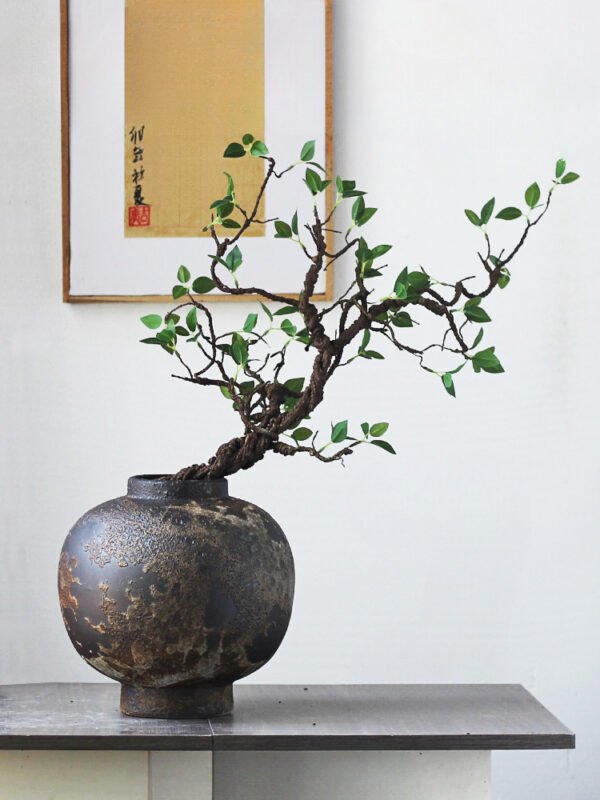 Rustic vase with bonsai near framed art piece.