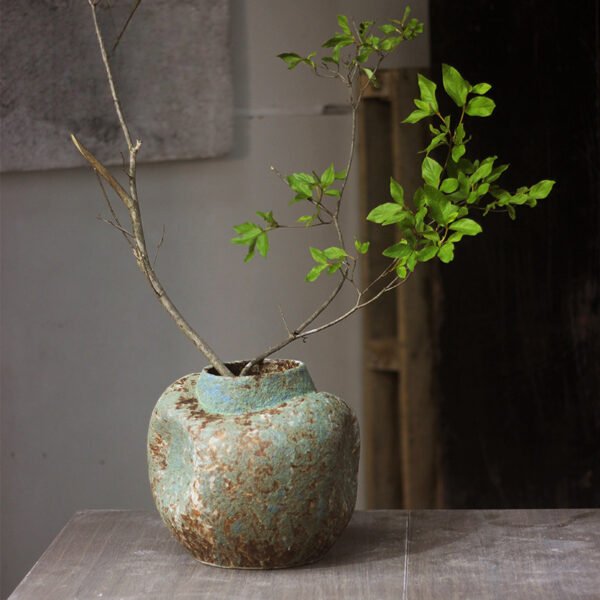 Rustic vase with green branches on table.
