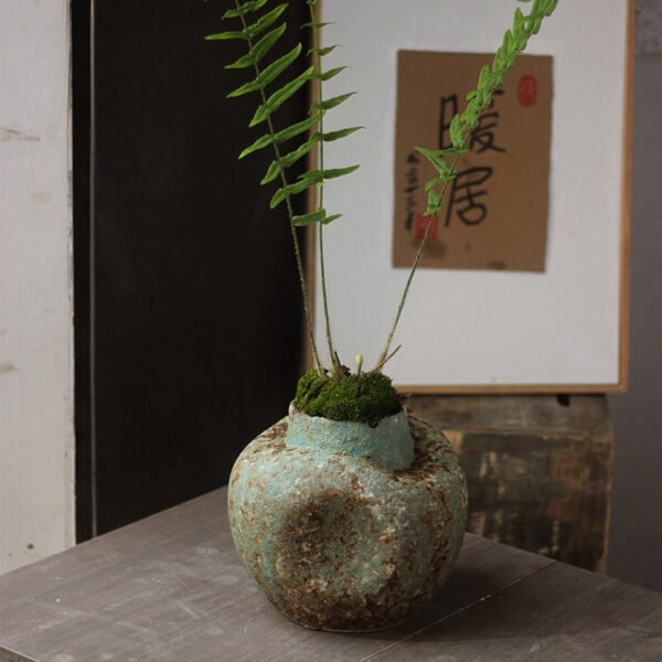 Rustic vase with fern and moss on table.