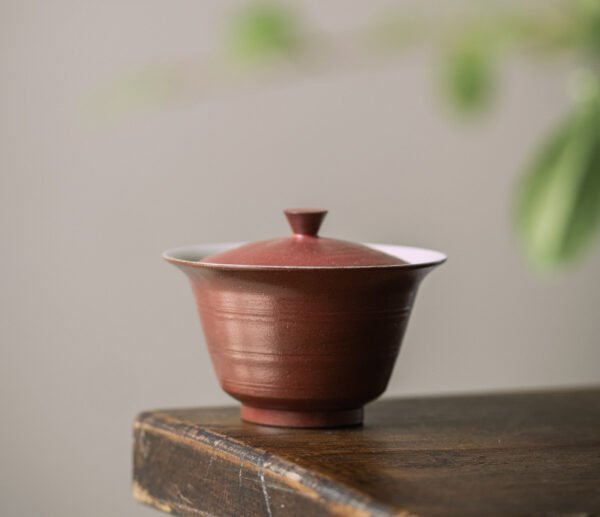 Red ceramic tea cup with lid on table.