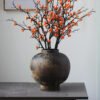 Rustic vase with orange berries on branches.