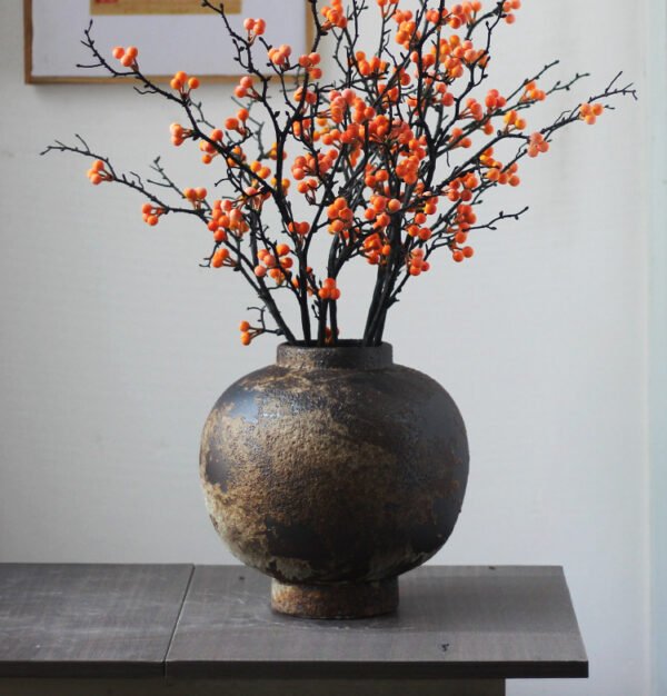 Rustic vase with orange berries on branches.