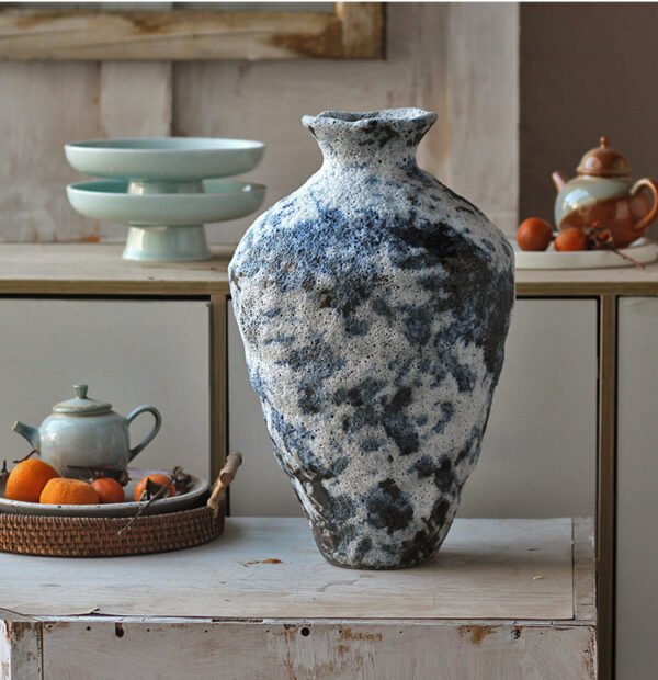 Textured ceramic vase on rustic table with teapot.